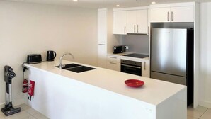 Una cocina moderna con armarios blancos, un refrigerador de acero inoxidable, un horno empotrado y una isla grande con un tazón rojo.