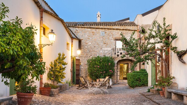 A cobblestone courtyard with stone buildings, a table with chairs, and potted plants. - Charming house with shared pool - Don Carlo (Buseto Palizzolo)