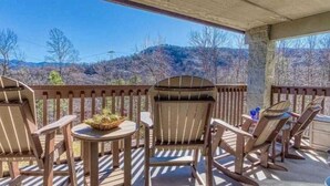 Uma área de estar coberta ao ar livre, com cadeiras Adirondack e uma pequena mesa, com vista para uma paisagem montanhosa.