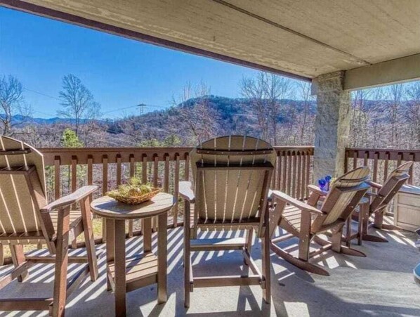 Un espacio al aire libre cubierto con sillas Adirondack y una mesa pequeña, con vistas a un paisaje montañoso.