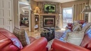 Uma sala de estar com lareira de pedra, sofás de couro e uma televisão montada acima.