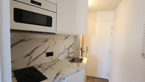A compact kitchen with a built-in oven, a marble backsplash, and a stainless steel sink.