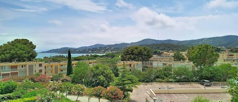 A residential area with buildings, a parking lot, and a view of the sea and hills.