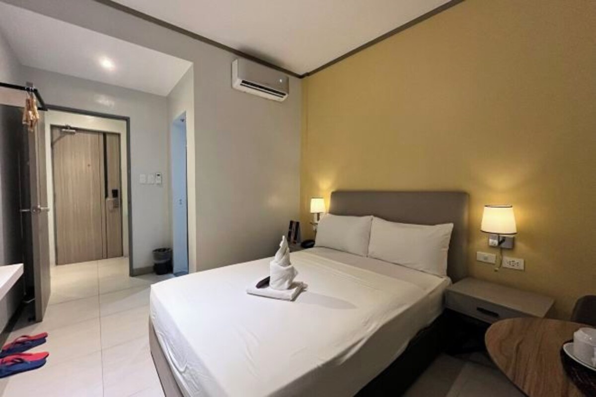 A hotel room with a bed, bedside lamps, a nightstand, a desk, and a bathroom.