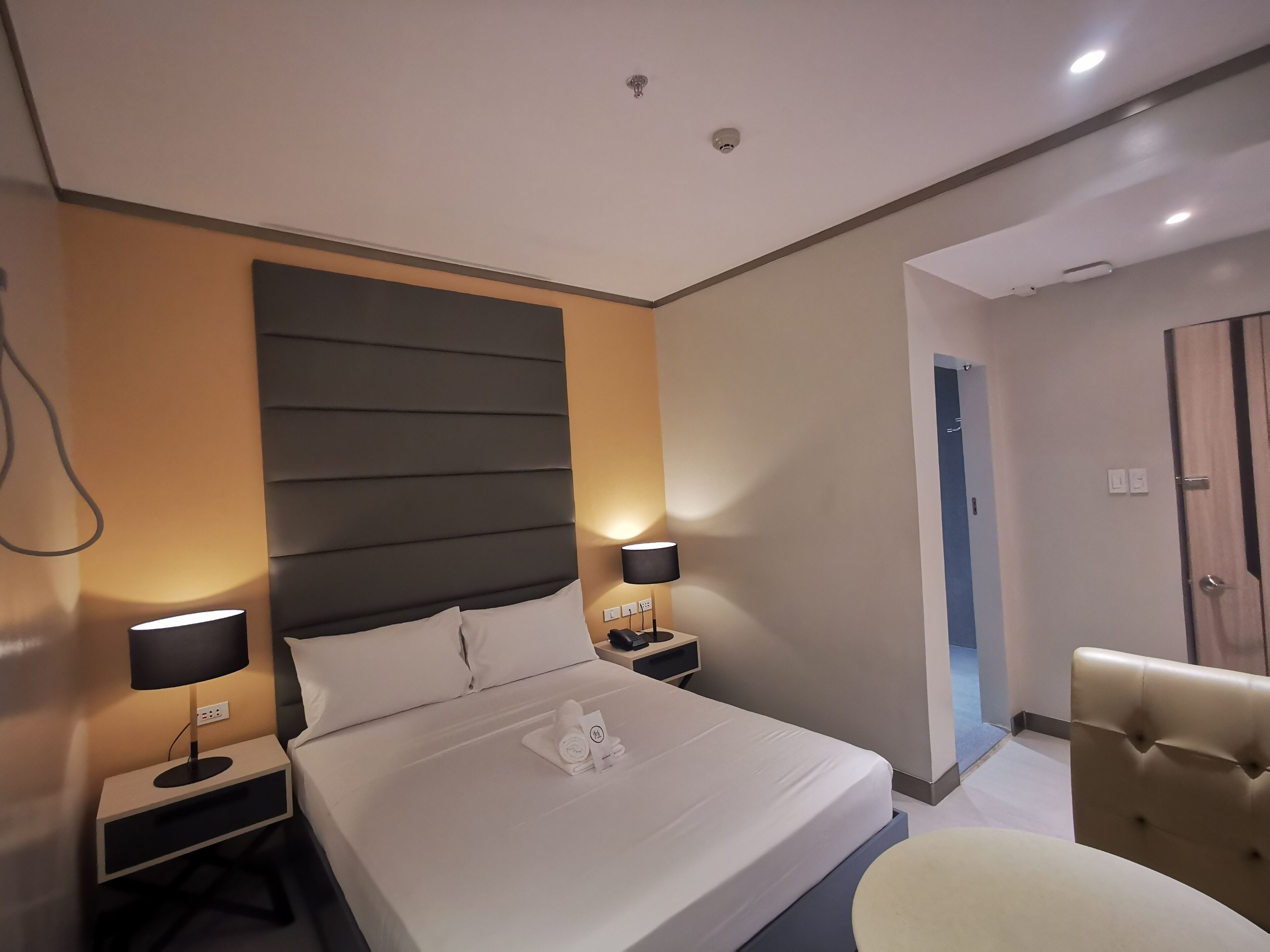 Ein modernes Hotelzimmer mit einem großen Bett, zwei Nachttischen mit Lampen, einer Kopfteil und einer Sitzecke mit einem Sessel.
