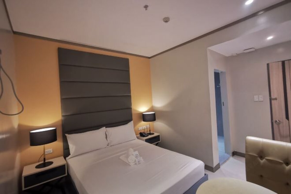 A hotel room with a large bed, two bedside tables, a headboard, and a chair.