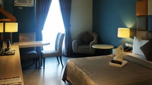 A hotel room with a bed, a desk, a chair, a small table, and a window with curtains. - Yes Hotel Pandi Bulacan (Pandi)