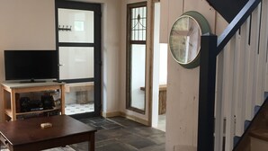 En stue med flisegulv, et træ sofabord, et fjernsyn på et stativ, en trappe med sort gelænder og en dør med sandblæst glas.