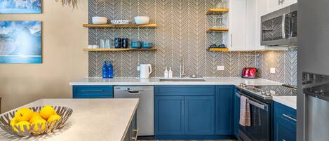 A modern kitchen with blue cabinets, a stainless steel refrigerator, and a wooden floor.