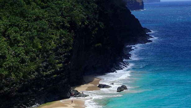 Un paisaje costero con una playa arenosa, aguas turquesas cristalinas y escarpados acantilados verdes.