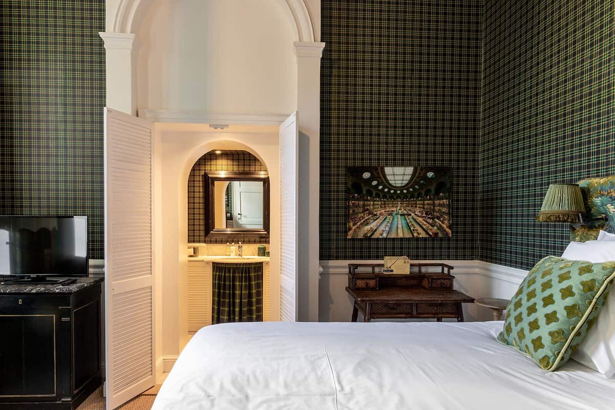 A bedroom with a large bed, a TV, a desk, and a painting on the wall.