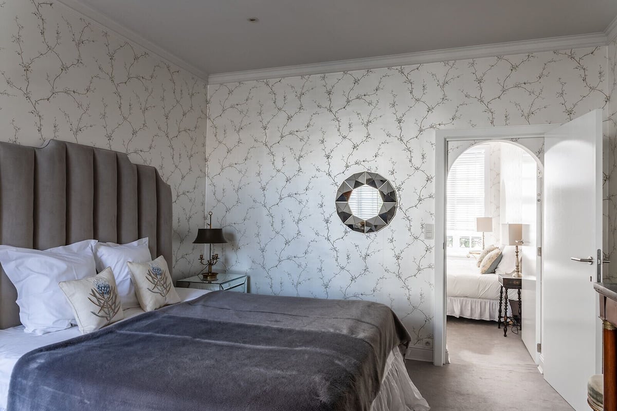 A bedroom with a bed, nightstand, lamp, and a wall-mounted mirror.