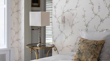 Une chambre à coucher avec un lit, une lampe, une petite table et un mur recouvert d’un papier peint à motifs floraux.