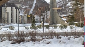 A view through an arched window of a snowy landscape with mountains, a modern building, and a unique sculpture. - studio near track and shopping mall (La Salle-les-Alpes)