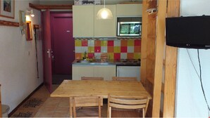 A compact kitchen with a wooden table and chairs, a purple door, and a tiled backsplash. - studio near track and shopping mall (La Salle-les-Alpes)