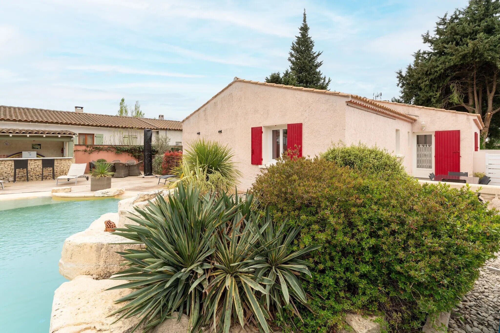 A building with red shutters, a pool, and surrounding greenery.
