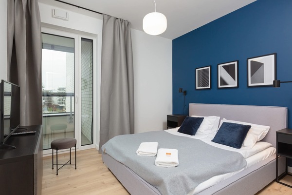 A cosy, bright bedroom with a double bed with grey headboard. One of the walls is in blue which adds a unique touch.
