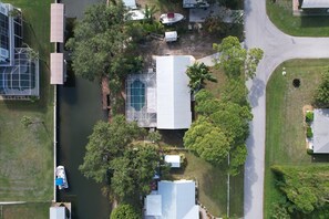 Ovenfra ses et boligområde med et stort hus, en swimmingpool og en bro med både.