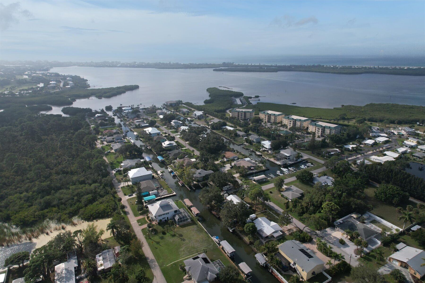 An aerial view of a coastal residential area with houses, a marina, and a large body of water.