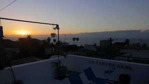 A rooftop terrace with a view of the sunset, potted plants, and the name 'LA CASITA AZUL' on the wall.