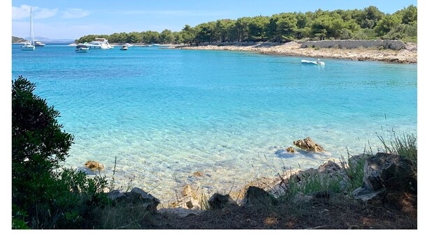 A coastal landscape with clear turquoise waters, boats, and a rocky shoreline.