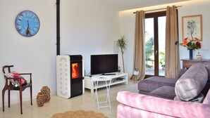 A living room with a television, a sofa, a chair, a clock, and a fireplace. - Son Alcaines Petit 249 cosy finca with private pool, terrace, barbecue and WiFi (Sineu)