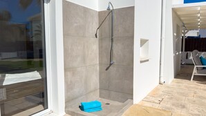 Un área de ducha exterior moderna con puerta de cristal, paredes con azulejos y una toalla azul en los escalones.