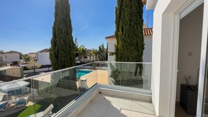 Un balcón con barandilla de vidrio que da a una piscina y un jardín.
