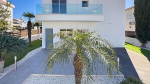 Una casa moderna de dos pisos con un balcón, un césped cuidado y una palmera en primer plano.