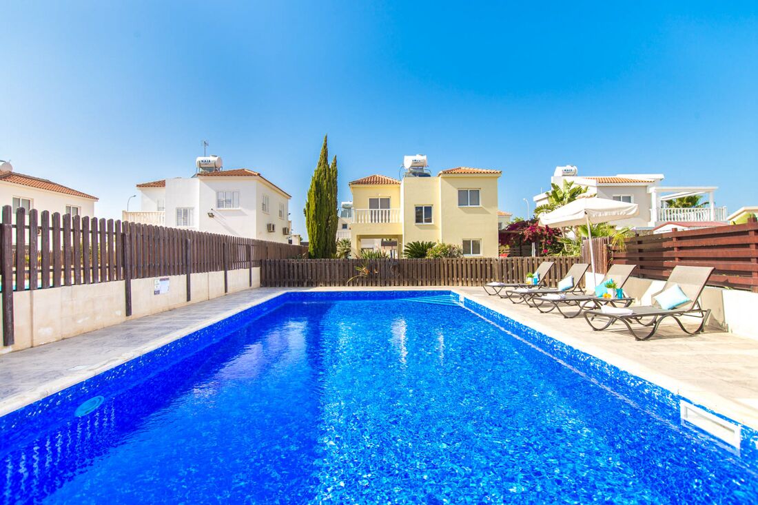 A swimming pool with lounge chairs and a wooden fence.