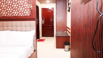 A narrow hallway with a bed on the left, a door at the end, and a trash can on the right.