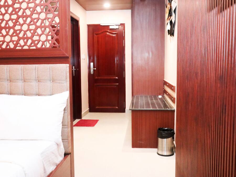 A narrow hallway with a bed on the left, a door at the end, and a trash can on the right.