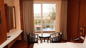 A hotel room with a bed, two chairs, a small table, a TV, and a balcony with curtains. - Mansha Palace (Port Blair)