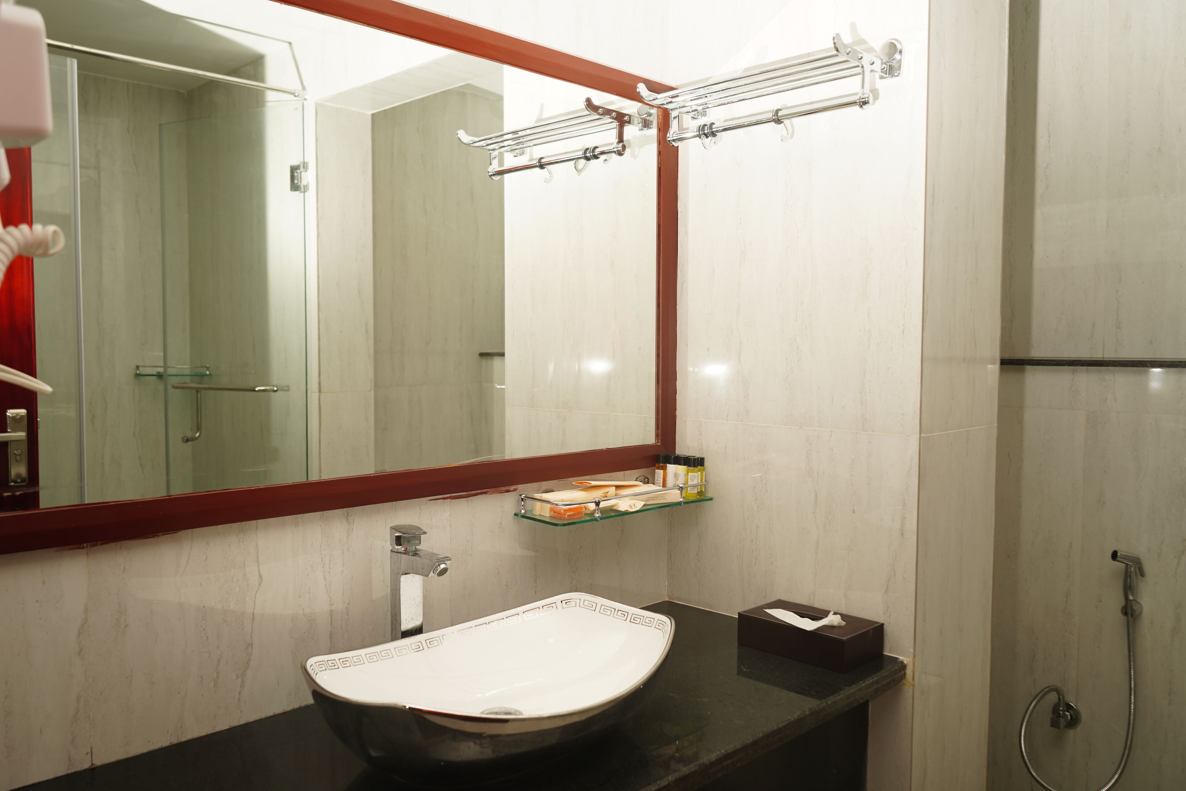 A bathroom with a large mirror, a white sink, a glass shelf, and a shower area.
