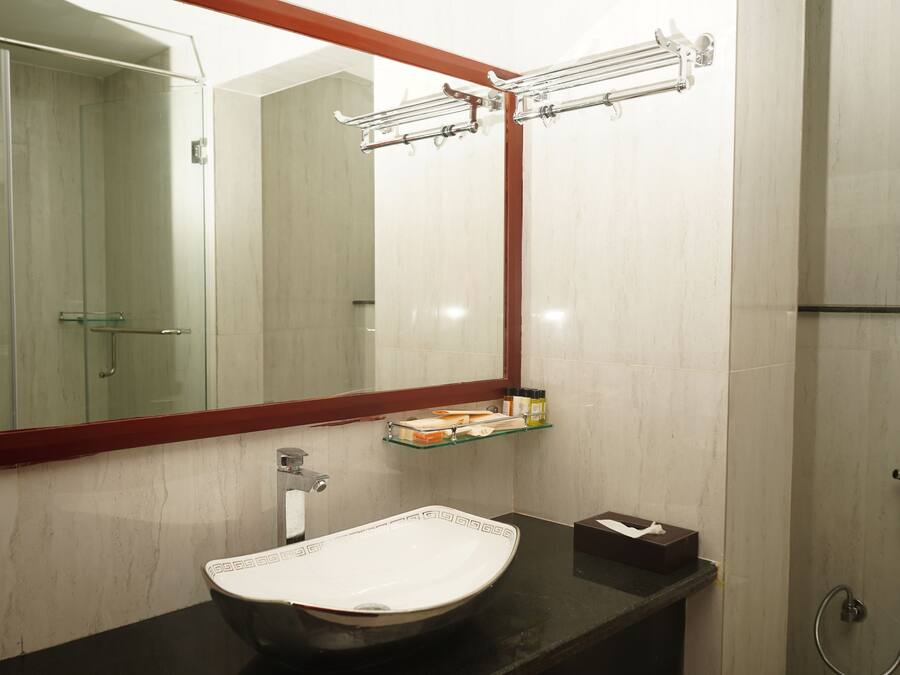 A bathroom with a large mirror, a white sink, a glass shelf, and a shower area.