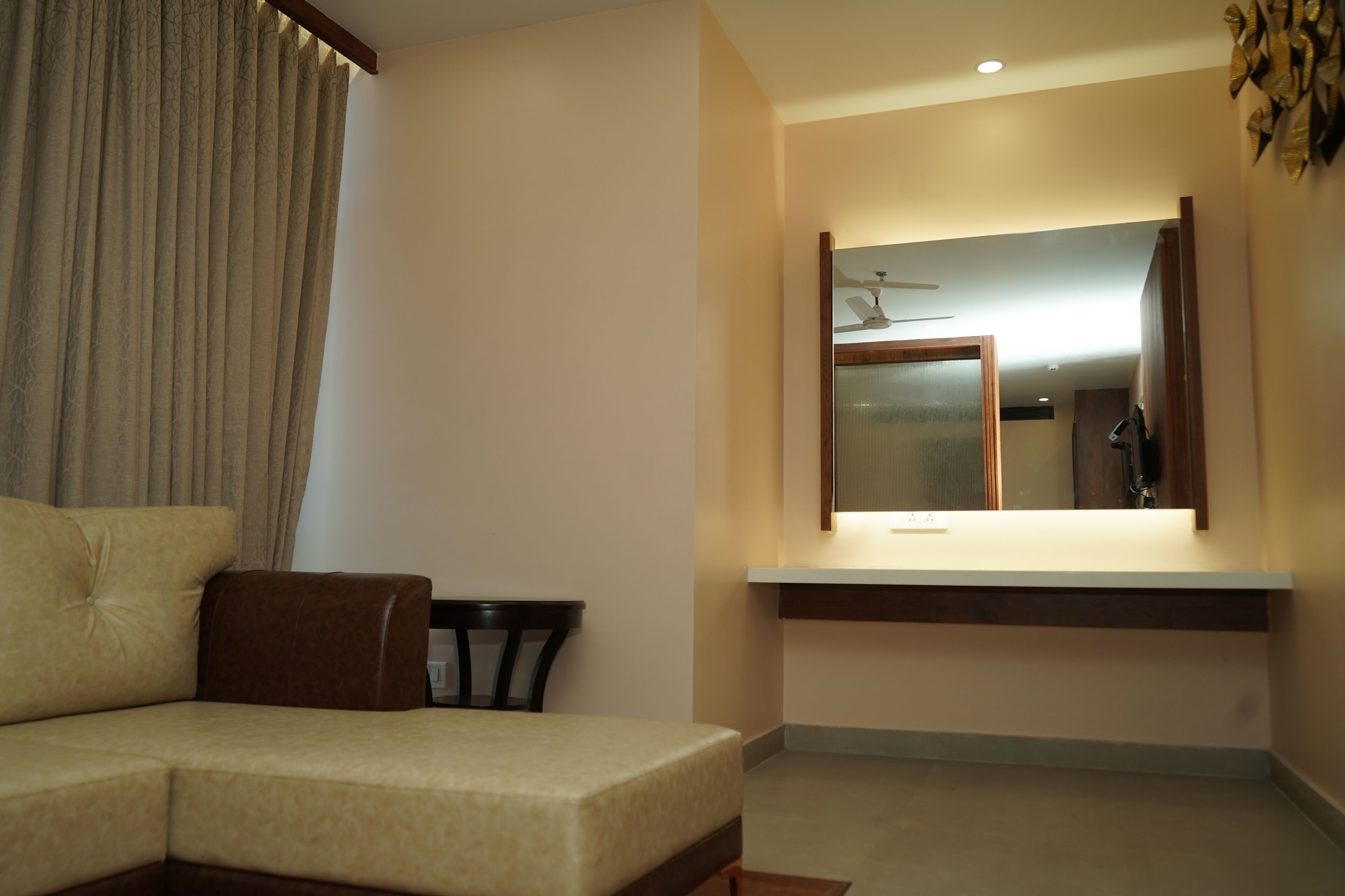 A modern hotel room with a sofa, a small table, a mirror, and a ceiling fan.