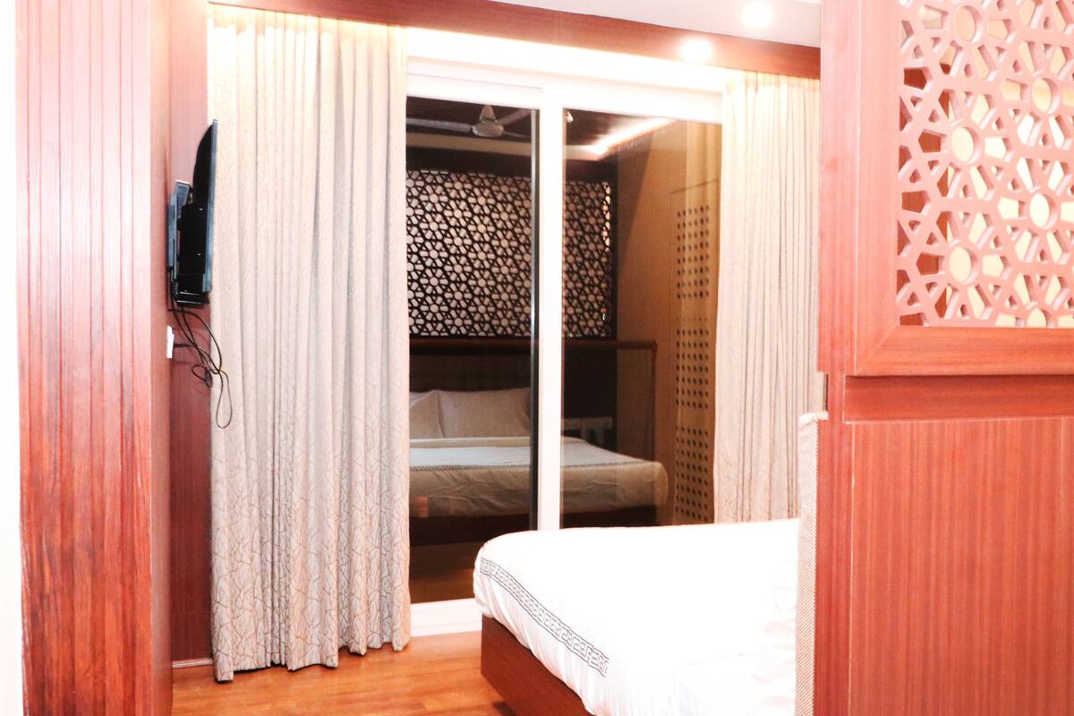 A hotel room with a bed, curtains, and a decorative wooden partition.