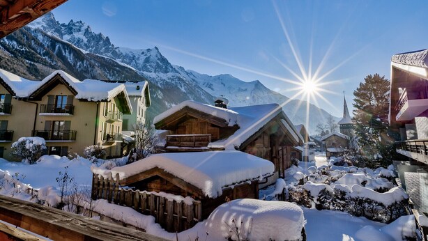 A snow-covered mountain village with wooden buildings, a church, and a clear view of the mountains.