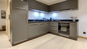 A modern kitchen with grey cabinetry, a built-in oven, and a stainless steel range hood.