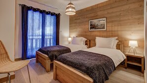 A double room with wooden panel walls, two beds with white linens, a woven chair, and a hanging light fixture.