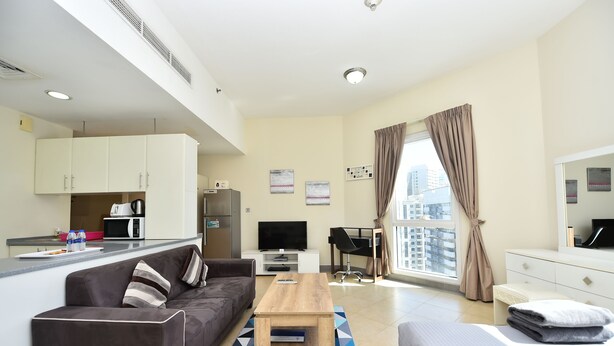 A modern apartment with a kitchenette, a sofa, a bed, a TV, and a large window with curtains. - Alia -Bright furnished studio near metro (Dubai)