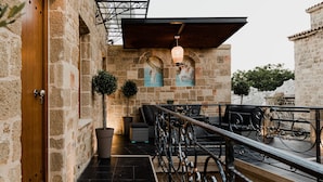 A stone-walled corridor with a wooden door, a small potted plant, a trash bin, and a metal railing. - Chateau Anax Hotel (Rhodes)