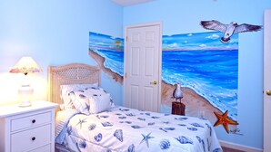 A bedroom with a bed, nightstand, lamp, and a wall mural of a beach scene.