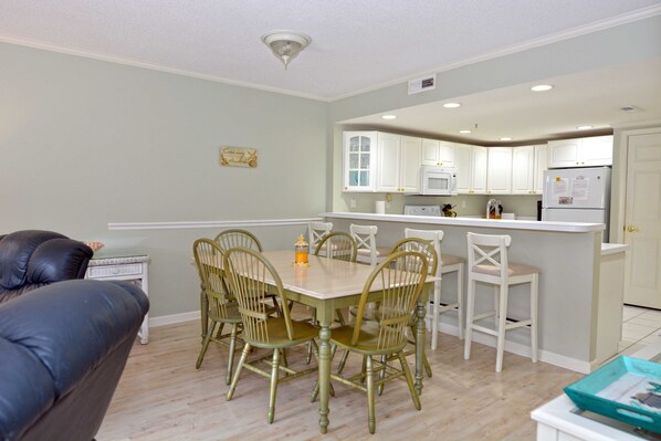 A dining area with a table and chairs, a kitchen in the background, and a leather couch.