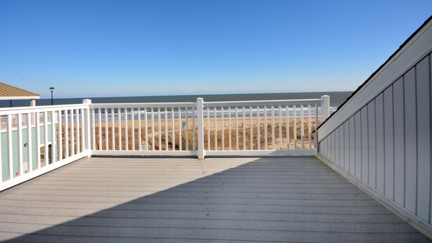 A wooden deck with a white railing overlooking a beach. - Beautiful, oceanfront 5 bedroom townhome! (Ocean City)