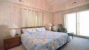 A bedroom with a large bed, two bedside lamps, a nightstand, a chair, and a window with curtains. - Beautiful, oceanfront 5 bedroom townhome! (Ocean City)