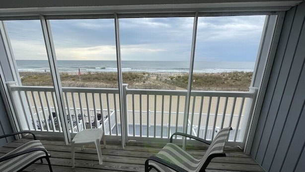 Ein überdachter Außenbereich mit Blick auf den Strand, ausgestattet mit einem Tisch und zwei Stühlen.