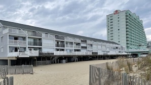 Ein Hotel direkt am Strand mit mehreren Balkonen, ein Sandstrand davor und ein Hilton-Gebäude im Hintergrund.