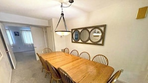 Ein Esszimmer mit Holztisch und -stühlen, einer Pendelleuchte und einem Wandspiegel.