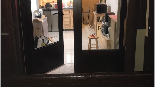 On aperçoit, à travers une porte à cadre sombre, une cuisine avec des meubles en bois, un four à micro-ondes et un tabouret.